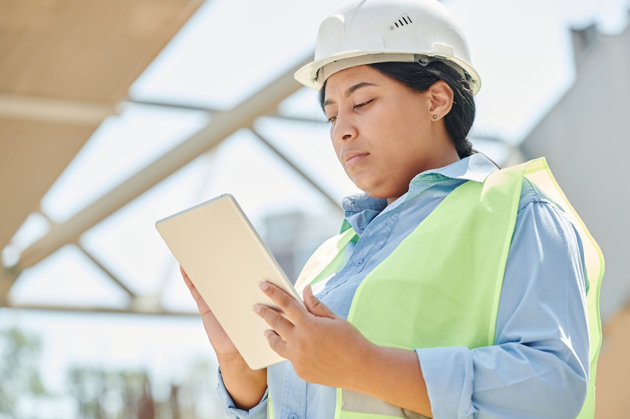 Confident female engineer in hard hat using a tablet computer at an outdoor construction site.